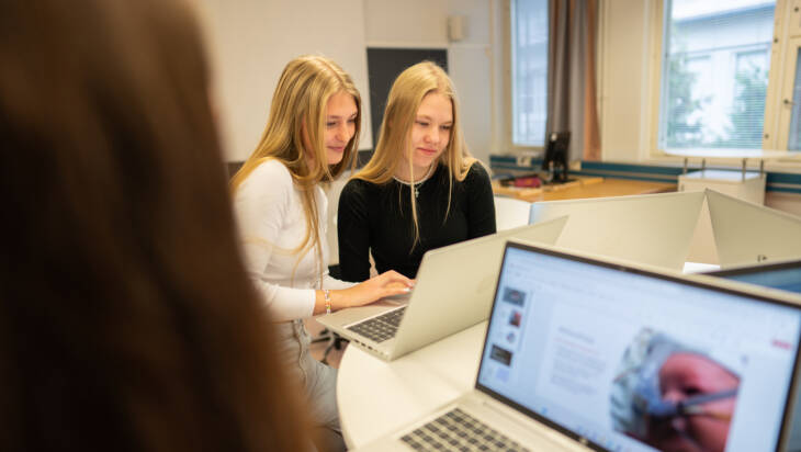 Kolme opiskelijaa luokassa opiskelemassa tietokoneila